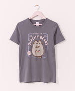 Pusheen Toe Beans Tee hangs on a light pink hanger on a light background. The medium grey tee shirt has a graphic of Pusheen the Cat lying on her back showing off her bottom pink toe beans.