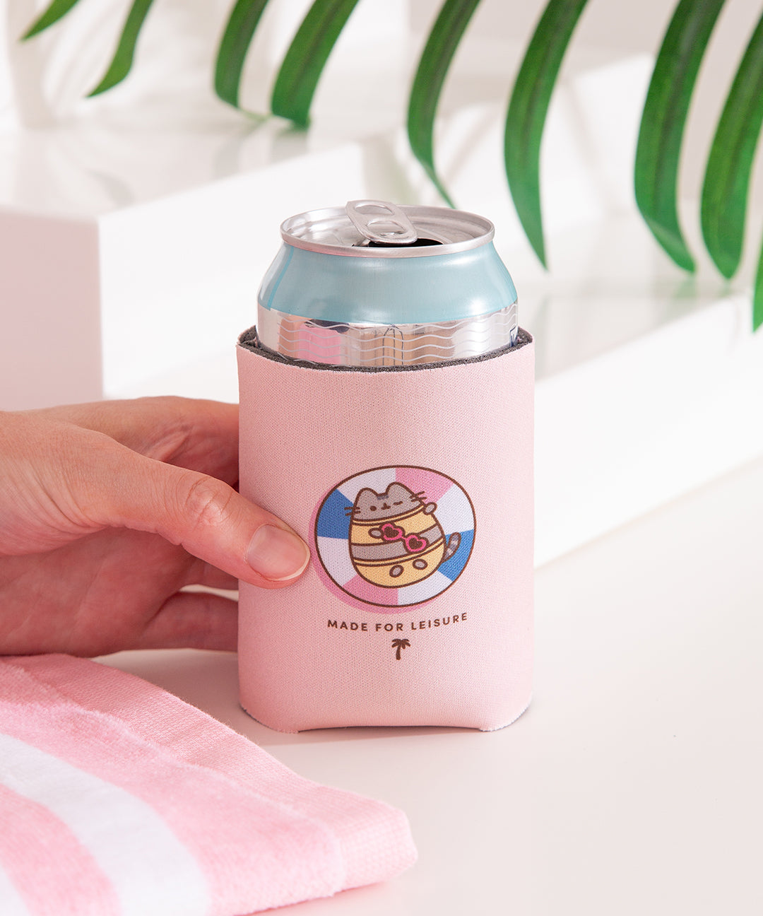 Model holds can with Pusheen drink sleeve with can inside. The front side of the coozie features a Pusheen graphic with the phrase "Made for Leisure" below.