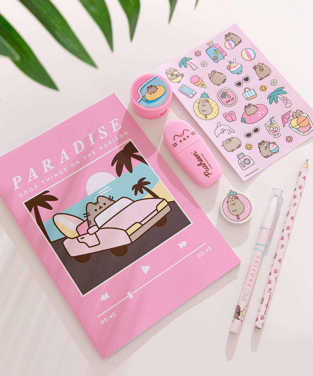 Contents of the Pusheen Tropical Vacation stationery set. The set includes a pink notebook, printed pencil, pencil sharpener, ballpoint pen, highlighter, stickers, and an eraser with tropical graphics on all items.
