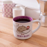 White Pusheen mug with purple interior sitting on a desktop with tea accessories.