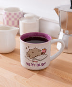 Pusheen Very Busy Mug is white with a purple interior and features Pusheen the Cat sleeping on papers.