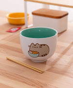 Pusheen Ramen Bowl sits on wooden table with the included chopsticks lying in front of the ceramic bowl.