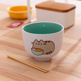 Pusheen Ramen Bowl sits on wooden table with the included chopsticks lying in front of the ceramic bowl.