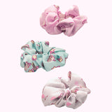 Side view of the Pusheen 3-Pack Hair Scrunchies. The trio includes light pink, mint green, and white scrunchies. Each scrunchie has a different all over print of Pusheen with various icons including hearts, stars, and more. 