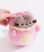 Front view of the Baby Pink Pusheen Year of the Dragon Plush. The grey fluffy Pusheen wears a fluffy light pink dragon costume with light yellow details on the horns, whiskers, collar, and belly. 