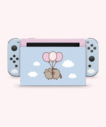 Front and back view of the Pusheen Balloons decal for a Nintendo Switch OLED. The front side is a two-toned light pink and light blue colors with a Pusheen graphic and white fluffy clouds. The back has blue joy stick stickers and a pink middle background with white fluffy clouds and a graphic of Pusheen in the middle of the decal being carried by three balloons.