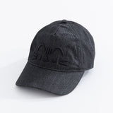   Left quarter view of Pusheen Black Denim Cap lying on a white surface. The black hat brim points towards the bottom left corner. The hat seams are in a black thread to match the charcoal hat color. 