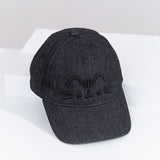 Top-down view of the Pusheen Black Denim Cap. The top button and seams can be seen from this view as well as the thread detailing on the bill of the hat. The hat is propped on a white box to show the full size of the baseball-style cap. 