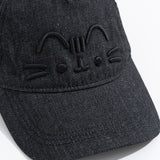 Close up view of embroidered graphic on the front center of the baseball style cap. Pusheen the Cat’s head stripes, ears, eyes, mouth and whiskers are shown in black embroidered thread. 