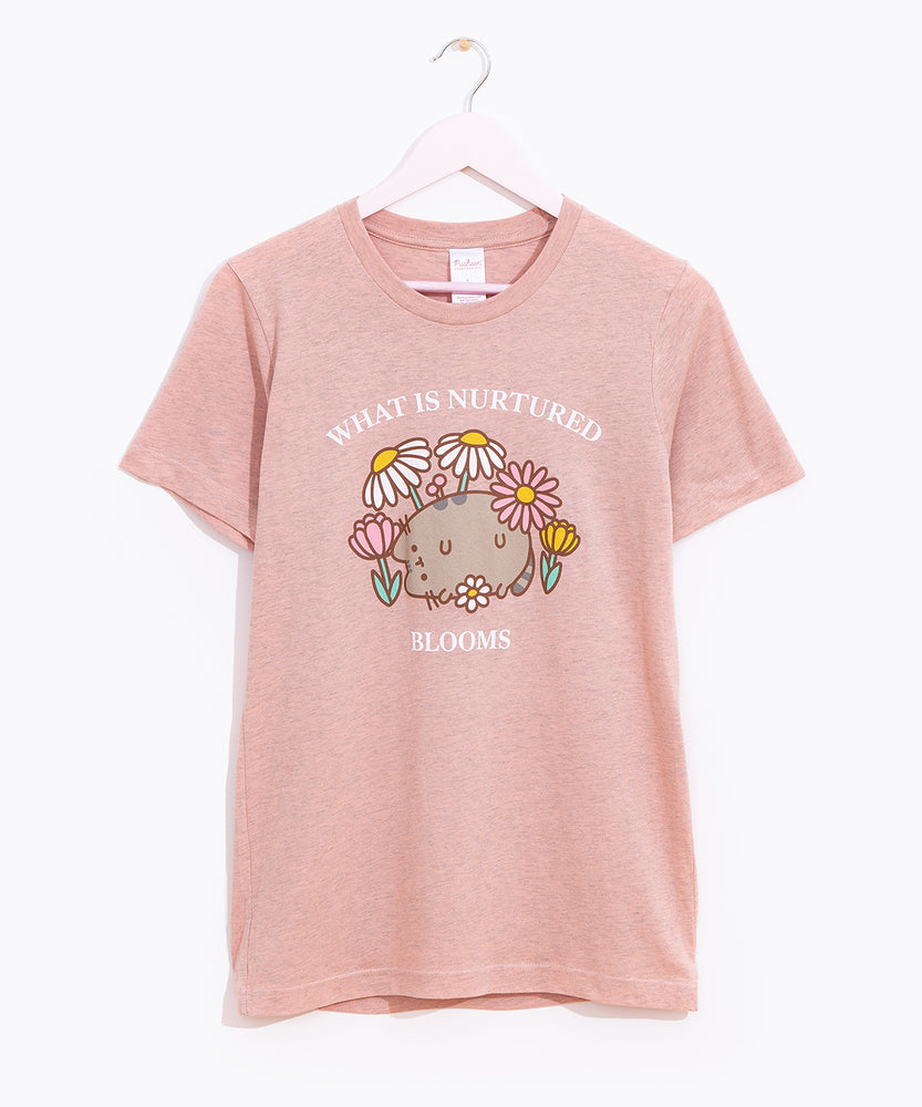 Pusheen Blooms Unisex Tee hangs on a light pink hanger in front of a white background. The graphic tee has a large print in the center of the t-shirt. 