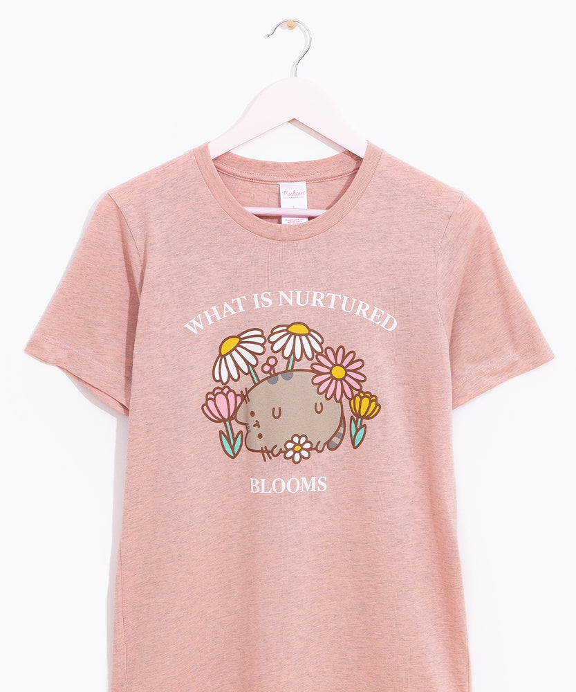 Pusheen Blooms Unisex Tee hangs on a light pink hanger in front of a white background. The printed graphic is placed in the front center of the shirt and covers most of the wearer’s chest. 