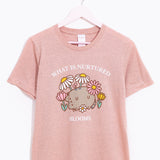 Pusheen Blooms Unisex Tee hangs on a light pink hanger in front of a white background. The printed graphic is placed in the front center of the shirt and covers most of the wearer’s chest. 