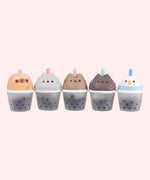 Line up of the Pusheen Boba Tea Surprise Squishy styles. From left to right is a yellow Sloth, light gray little sister Stormy, a gray Pusheen the Cat, a dark grey little brother Pip, and a blue and white Bo the Parakeet.