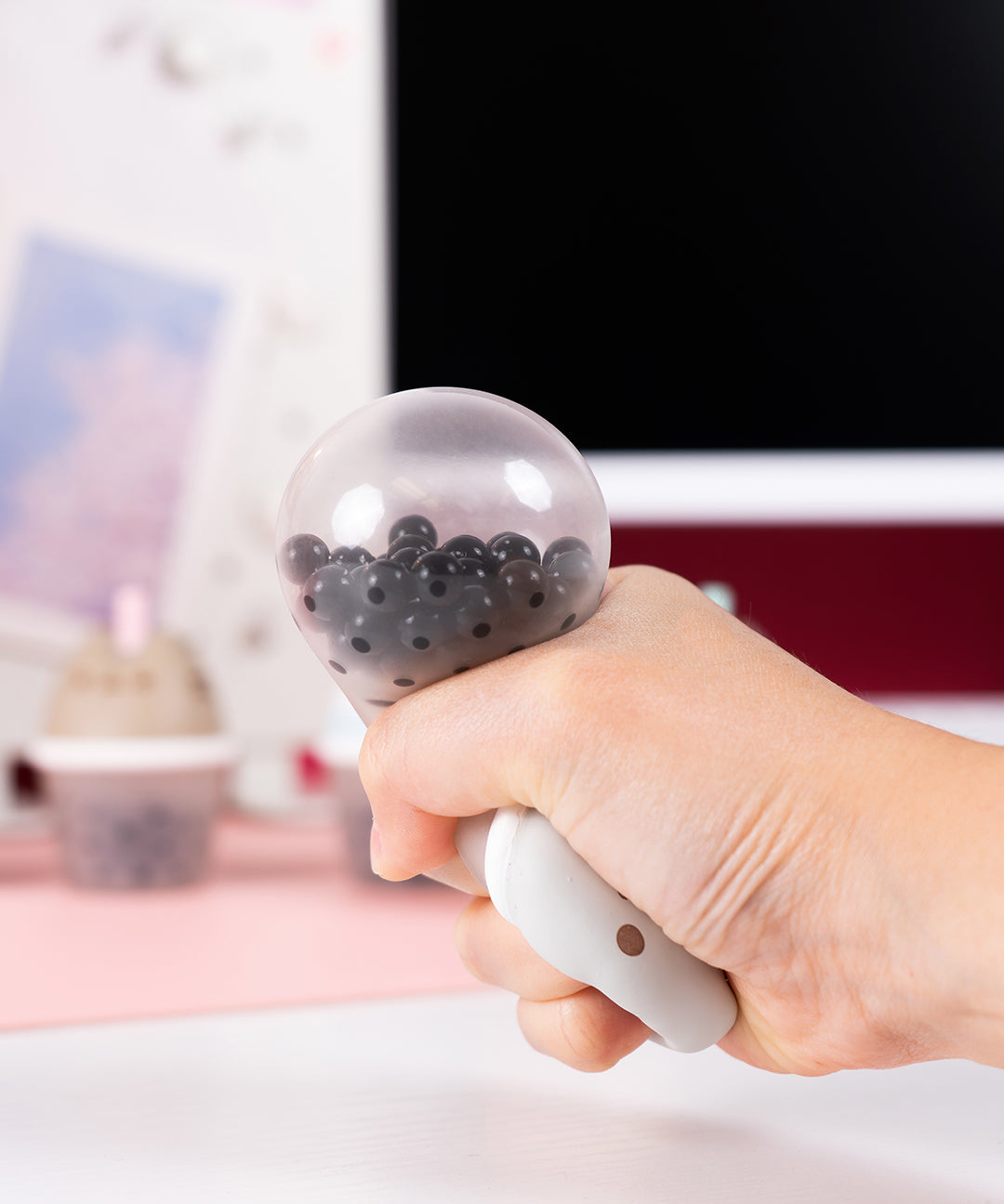 Model squishing the Pusheen Boba Tea Surprise Squishy. The bottom half of the toy is translucent and has black beads inside to mimic boba pearls. 