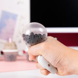 Model squishing the Pusheen Boba Tea Surprise Squishy. The bottom half of the toy is translucent and has black beads inside to mimic boba pearls. 