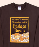 A chocolate brown sweatshirt with the sleeves folded lies against a light-yellow background. The unisex sweatshirt has a screen-printed graphic on the center of the chest. The graphic depicts a magazine cover showcasing “the wondrous world of Pusheen Breads.” This is a special, first edition cover featuring Loaf Pusheen, Baguette Pusheen, Croissant Pusheen, Loaf Pusheen, and Sesame Bagel Pusheen in golden shades of baked goodness. 