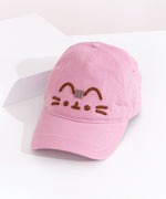 Left quarter view of Pusheen Cap lying on a white surface. The light pink hat brim points towards the bottom left corner. The hat seams are light pink to match the light pink hat color. 