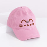 Right quarter view of Pusheen hat lying on a white surface. The cap curved brim points towards the bottom right corner. The hat is propped on a white box to show the full size of the baseball-style cap. 