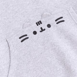 A close-up view of the embroidered graphic on the front pocket of the sweatshirt. The classic Pusheen pose shows her whiskers, mouth, eyes, head stripes in a dark gray thread. The cat’s rounded triangle ears are made of the same fabric as the hoodie and are a 3D feature of the hoodie. 