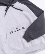 Front view of the Pusheen Relaxed-Fit Character Hoodie lying on a white surface. The two-toned sweatshirt has a dark charcoal grey hood and sleeves while the chest and bottom of the sweatshirt are light heather gray. 