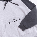 Front view of the Pusheen Relaxed-Fit Character Hoodie lying on a white surface. The two-toned sweatshirt has a dark charcoal grey hood and sleeves while the chest and bottom of the sweatshirt are light heather gray. 