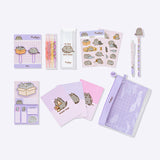 Contents of the Pusheen Deluxe stationery set in front of a light purple background. The set includes two paperclips, highlighters and case, two sticker sheets, a ballpoint pen, pencil, eraser topper, sticky notes, 3 notebooks, and a pouch to hold it all.