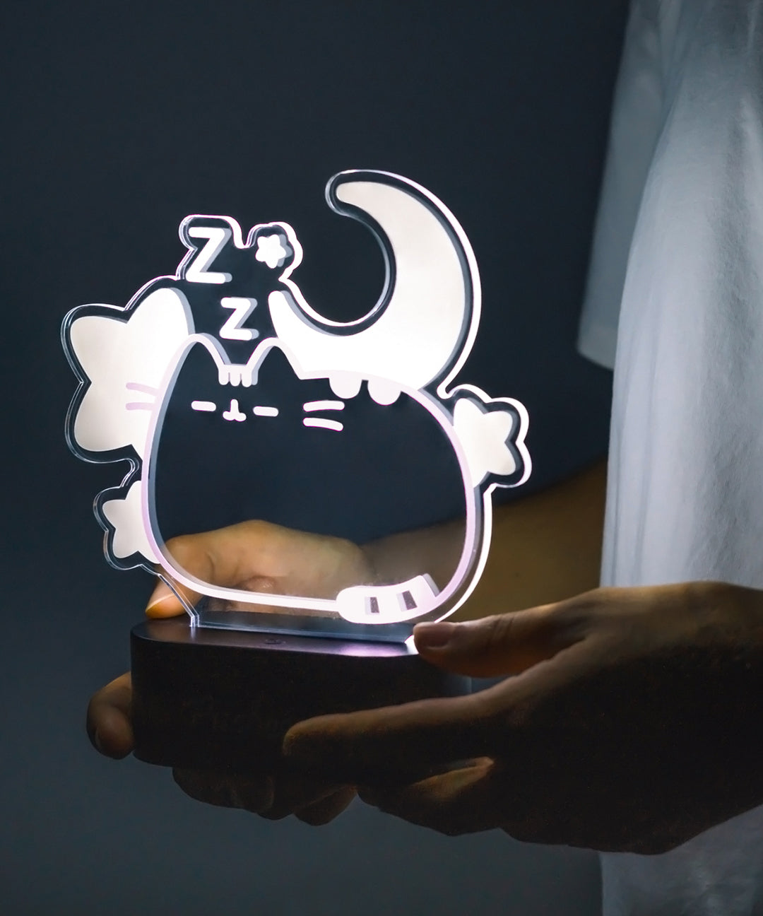 Model holding Pusheen Lamp to show size of lamp. The cat is surrounded by stars, a crescent moon, and zz's. The cat body gives off a light purple glow.