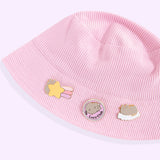 Three Pusheen pins attached to a light pink bucket hat. The gold-foiled pins show the grey and brown tabby cat having a dreamy day. 