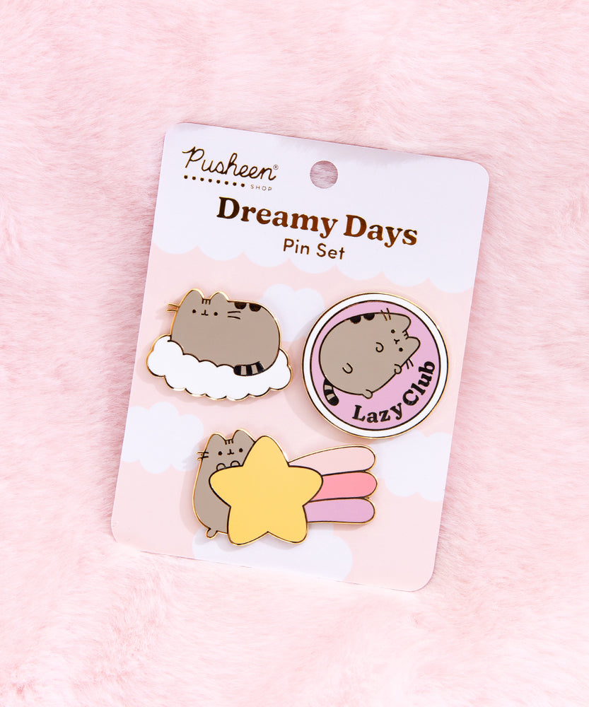 The pin set is attached to a cardboard backing featuring white fluffy clouds on a light pink background. The pin set is lying on a white light pink background. 