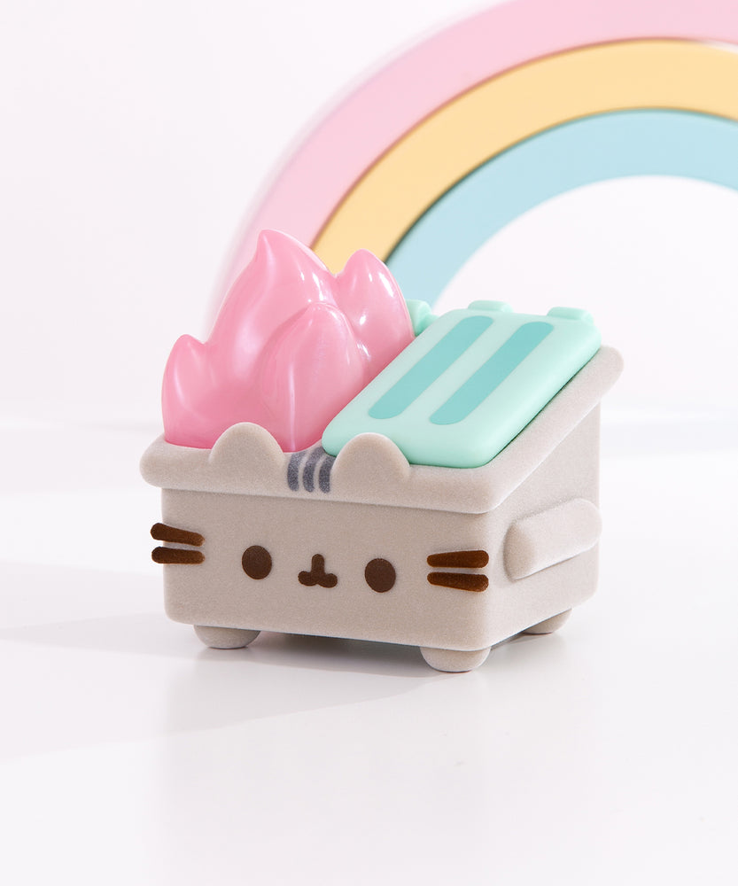 Front and side view of the vinyl figure in collaboration with 100% Soft and Dumpster Fire. The small Pusheen collectible stands on four legs, has a fuzzy grey body, and pastel-pink flames extending off the top of the toy.  
