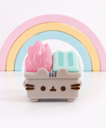 Front view of the Pusheen trash can in front of a pastel-colored rainbow. The small figurine includes Pusheen’s ears extending off the front top of the figure.  