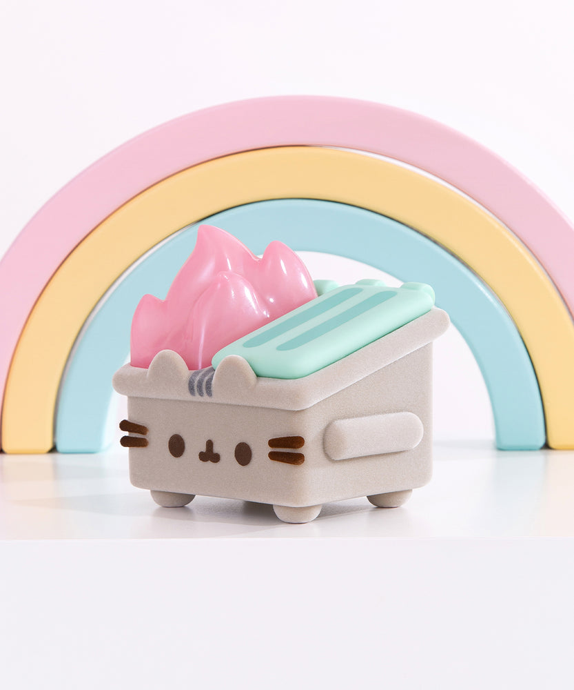 Front and side view of the Pusheen toy. The grey fuzzy dumpster sits on four legs, has side handles, and mint green top lids. On the front of the toy is Pusheen’s face in brown fuzzy, 3D flocking. Coming out of the top of the toy figure is pastel pink flames.  