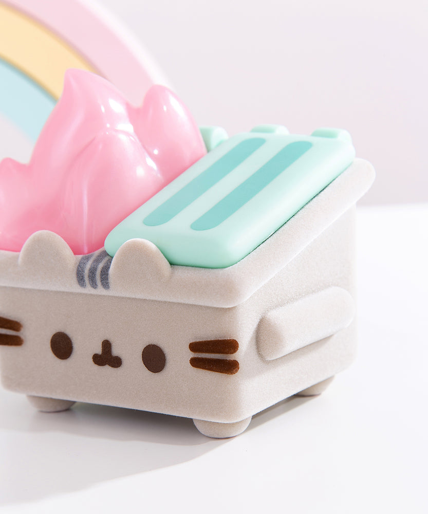 Close-up view of the front and side of the Pusheen Dumpster Fire Vinyl Figure. The fuzzy grey body is accompanied by plastic pink flames and a mint green trash lide. Pusheen’s brown and grey eyes, mouth, and whiskers are added on top of the front of the trash can. 