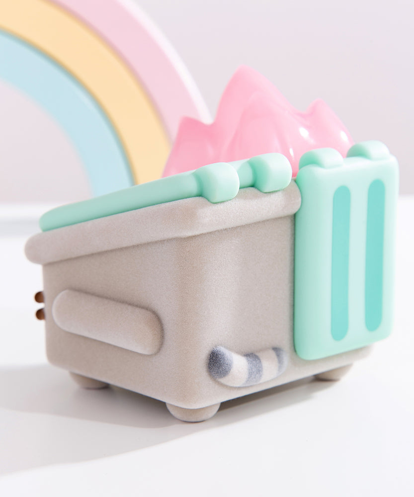 Front and side view of the Pusheen toy. The grey fuzzy dumpster sits on four legs, has side handles, and mint green top lids. On the front of the toy is Pusheen’s face in brown fuzzy, 3D flocking. Coming out of the top of the toy figure is pastel pink flames.  