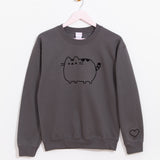 Pusheen Embroidered Unisex Sweatshirt hangs on a light brown hanger in front of a white wall. The charcoal sweatshirt features Pusheen embroidered in a black thread on the front of the sweatshirt with a heart outline embroidered on the wearer’s left sleeve near the cuff. 