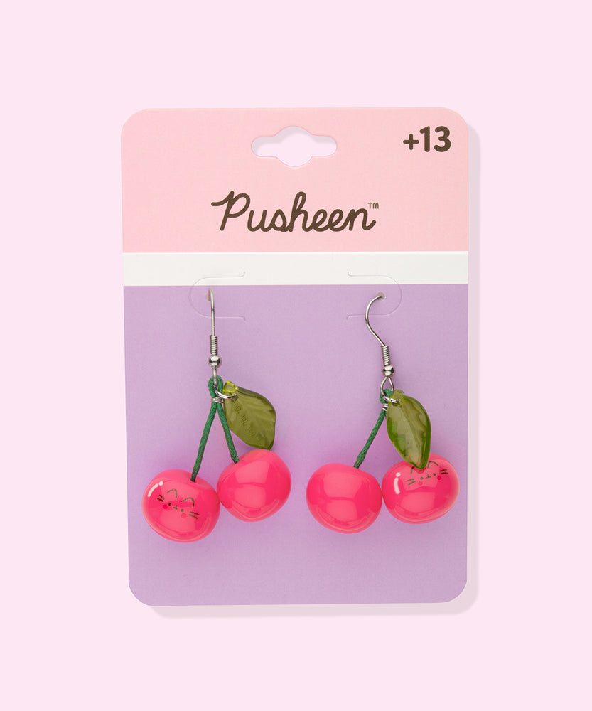 Pusheen Fruits Cherry Dangle Earrings on their cardboard backing card. The top half of the card has the Pusheen logo in brown on a light pink background and the bottom half of the card is purple. 