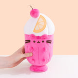 Model holds the side of the Parfait Pusheen Plush. The hot pink body is accompanied by vertical pink lines to imitate a classic glass container. Pusheen's head stripes, eyes, smiling, mouth and whiskers are embroidered on the front of the plush while her hot pink ears and paws extend off the plush body.   