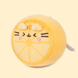 Left quarter view of the yellow-colored Pusheen Squisheen. On the front of the plush are six light yellow triangles arranged in a circle to mimic the look of the inside of a lemon. 