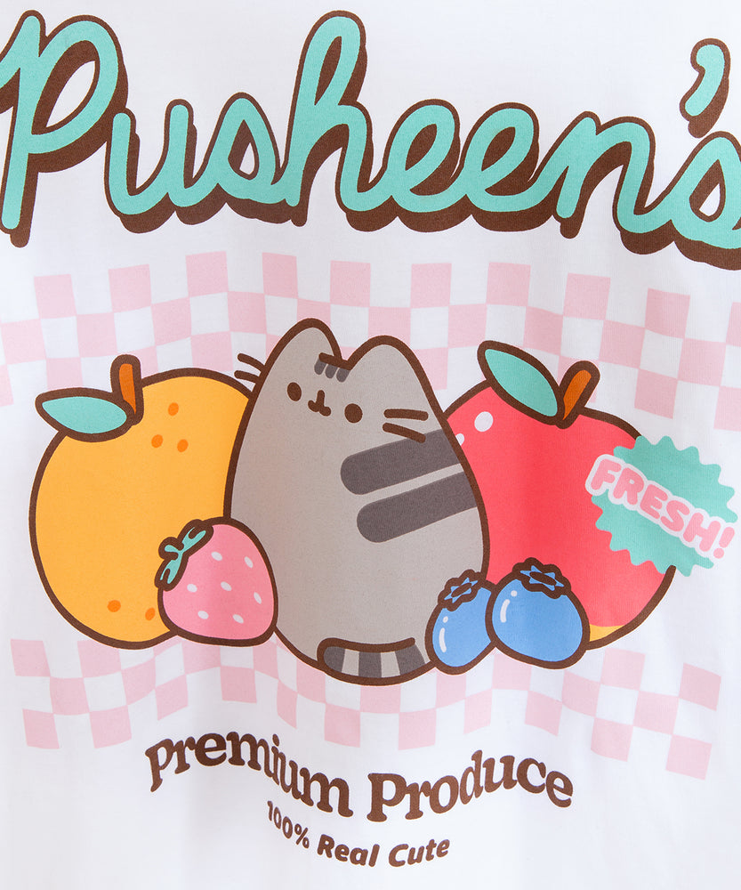 Close-up view of Pusheen fruits graphic tee. The multi-colored large front graphic features mint green, light pink, orange, blue, red, and brown. Included in the artwork is the phrase “100% Real Cute” in brown and a sticker badge that says “Fresh!” in mint green and pink. 