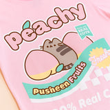 A close-up view of the Peachy Fruits Unisex Tee's screen print graphic. Pusheen sits in between two peaches with her back to the viewer and her looking over her shoulder. On the tee include the phrases “peachy,” “made with real cute,” “pusheen fruits,” “fresh,” and “100% Real Cute.” All print elements include the colors Grey, yellow, pink, green, and white. 
