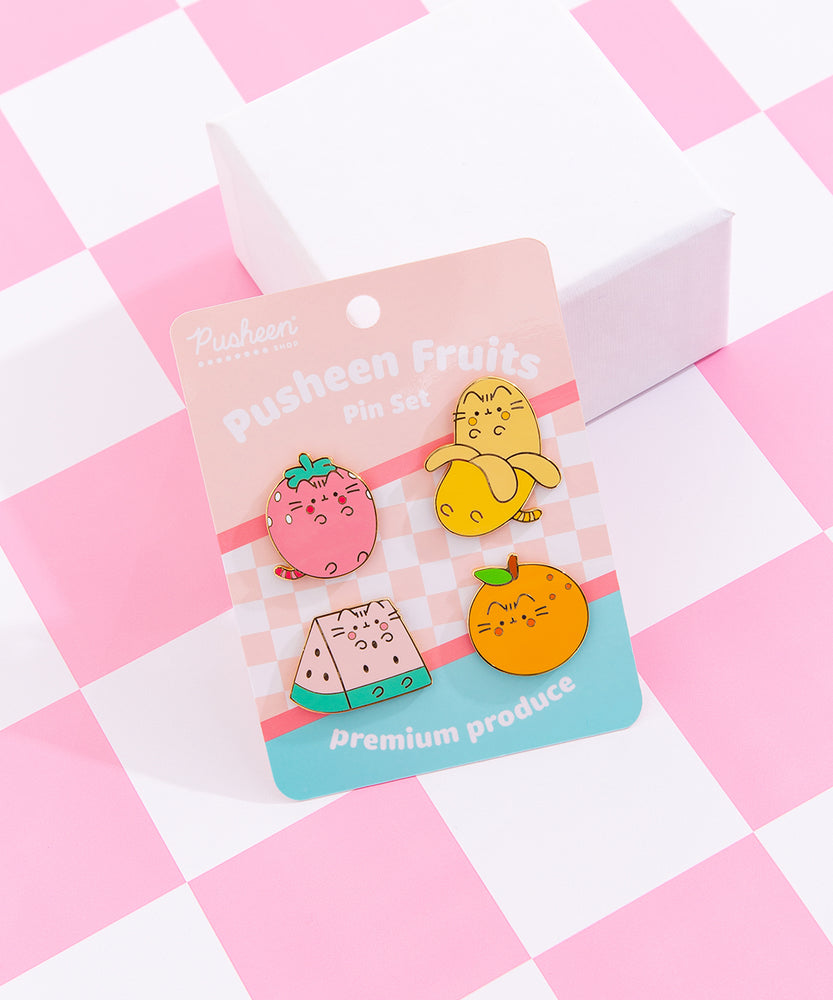 Front view of the Pusheen Fruits Pin Set. The set includes four pins of Pusheen as fruits including a pink strawberry, yellow banana, pink and green watermelon slice, and an orange.
