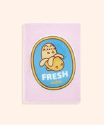 Front cover of the Pusheen Fruits Plush Notebook. On the center of the pink notebook is a PVC patch of Pusheen the Cat as a yellow banana in front of a blue background with a yellow border. Under the banana graphic is the word "Fresh" and the banana grocery code "#4011."