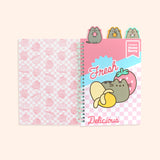 The cover of the notebook opened to the first page. The interior cover features a pink all over pattern of Pusheen as various Fruit characters in front of a pink checkered background. The first page has a pink patterned background with a graphic of Pusheen with a partially peeled banana and a pink strawberry surrounded by the phrases “fresh,” “premium strawberry,” and “delicious.: The pattern page is attached to the tab of Pusheen holding a pink strawberry.