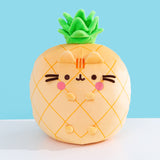 Front view of the Pusheen Fruits Scented Pineaplle Squisheen Plush. Pusheen the Cat is a yellow pineapple with a vibrant green crown that’s sitting atop a white tabletop.