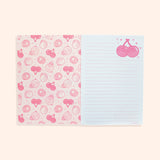 Interior view of stationery notebook. The protective first page is shades of pink and features a pattern of Pusheen as various fruits including pineapple, kiwi, cherry, and lemon. The next pages show the white with pink-lined interior writing pages.