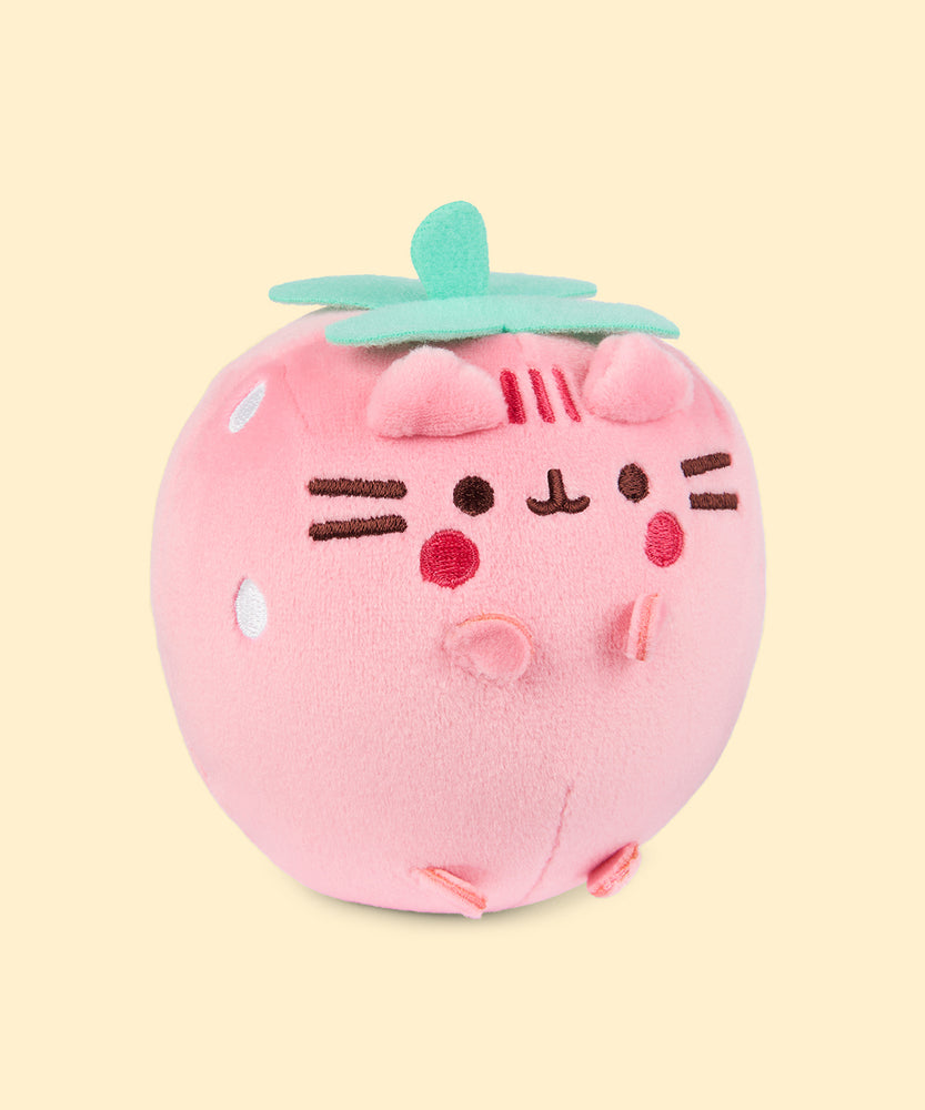 Back view of the Pusheen Fruits Strawberry Squisheen Plush. On the back of the light pink squisheen is Pusheen’s signature back stripes duo embroidered in dark pink. Under the stripes is Pusheen’s striped tail in alternating pink colors. Coming off the top of the plush are green felt leaves and a stem. 