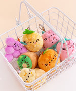 Front view of Pusheen Fruits Surprise Plush assortment. Pusheen the Cat has taken the form of seven miniature fruit-inspired plushes. At the top left is the packaging box for the Pusheen Fruits surprise plush. From left to right and top to bottom, the surprise plush are a strawberry, half-peeled banana, pineapple, grape cluster, watermelon slice, cut kiwi, and an orange. The bottom right corner has a burst with the words “1 Mystery Design” indicating eight possible miniature plush keychains are available. 