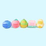 Line up of the Pusheen Fruits Surprise Squishy. From left to right is a blueberry, strawberry, pear, watermelon slice, and partially-peeled banana. In this view, the backs of the squishys can be seen. Each squishy features Pusheen's two back stripes and striped tail in matching colors to the respective squishy.