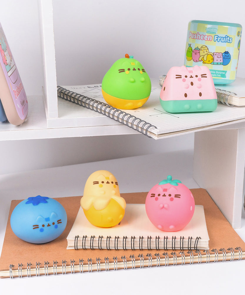 Pusheen Fruits Surprise Squishys sit atop desk shelves. Each squishy (except blueblerry) feature Pusheen's four paws extending slightly off the front of the 3D figure.