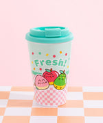 A pink and mint travel mug with a mint green lide. The mug has a pink checkered print on the bottom and mint on top. The front graphic of the Travel Mug includes Pusheen as various fruits characters including a winking pink peach, a shiny red apple, and a relaxed green pear. The phrase “Fresh!” is above the fruit graphics in mint green and is surrounded by orange, red, and green confetti. 